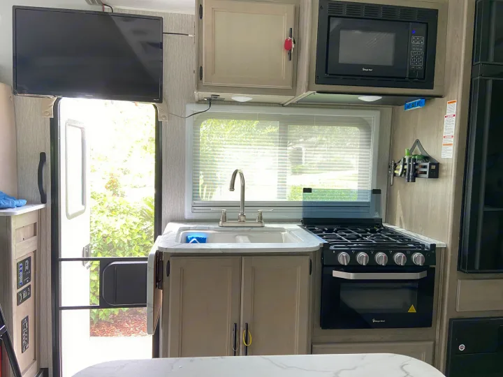 A well-equipped RV rental kitchen with a sink, stove, microwave, and TV, offering a cozy space for mobile adventures.. Mercedes-Benz Sprinter Coachmen Prism 2021