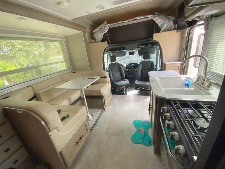 Bright RV rental interior showing a U-shaped dinette, kitchen with stove/sink, and driver's cockpit. Ideal for travel.. Mercedes-Benz Sprinter Coachmen Prism 2021