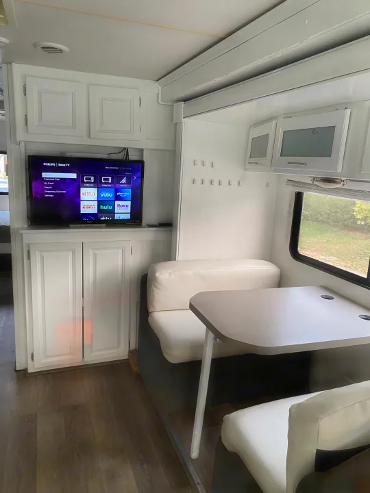 Modern RV rental interior showing a compact dining area, wall-mounted Roku TV, and white storage cabinets. Ideal mobile living.. Forest River Georgetown 2011