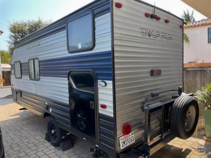 This modern Wolf Pup travel trailer, a compact RV rental, is pictured from its side & rear, ready for your next trip.. Forest River Cherokee Wolf Pup 2022