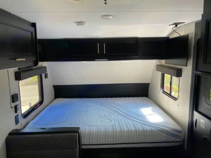 Inside an RV rental: a compact bedroom features a comfortable mattress, overhead storage, and mounted TV for your journey.. Forest River Cherokee Wolf Pup 2022