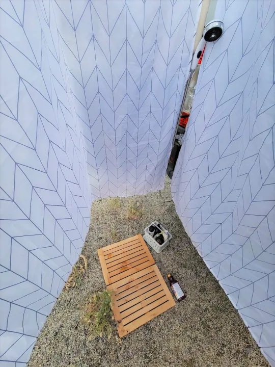 Private outdoor shower for your RV rental adventure: patterned curtains, wooden mat, and toiletries on a gravel ground.. Dodge Promaster 2500 High Roof 2020