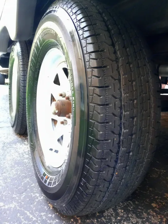 New-looking tires and white wheels on an RV rental, parked on asphalt, ready for adventure.. Holiday rambler Traveler 2013
