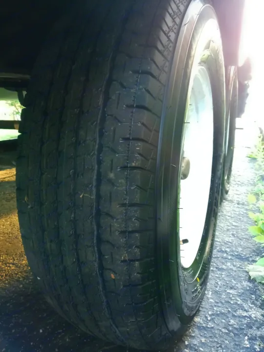 Close-up of a multi-axle RV rental tire, showing healthy tread and white rim on asphalt.. Holiday rambler Traveler 2013