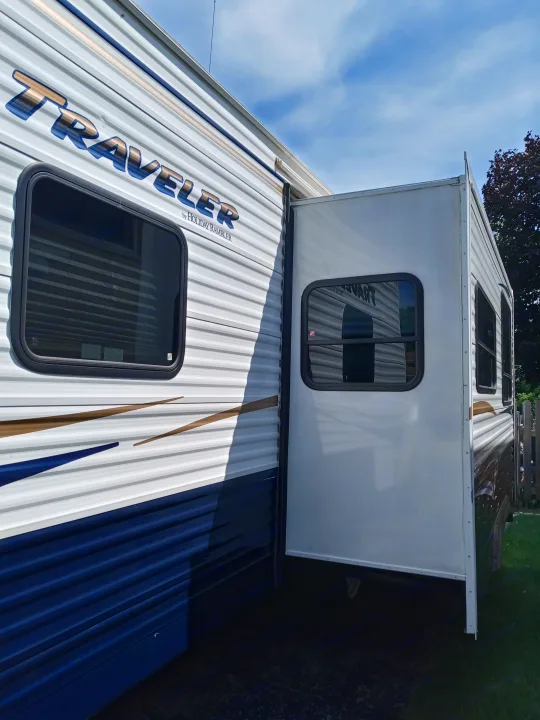 Side of a white 'TRAVELER' RV with an extended slide-out and windows, parked outdoors. Perfect for your next rv rental.. Holiday rambler Traveler 2013