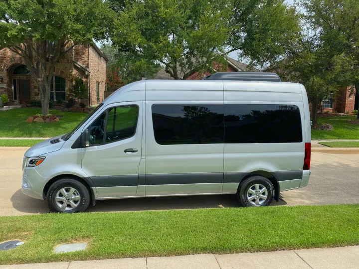 A sleek silver Mercedes-Benz Sprinter van, likely an RV rental, is parked curbside in a suburban setting.. Mercedes-Benz Sprinter 2021