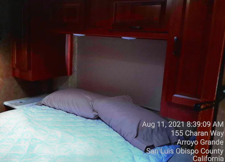 RV rental bedroom interior: a bed with light blue quilt, two beige pillows, and dark wood overhead cabinets.. Forest River Sunseeker 2018