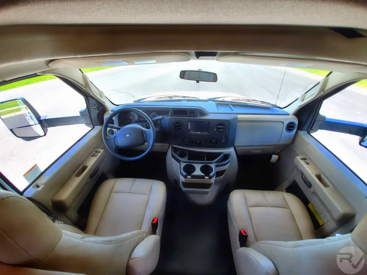 Spacious RV rental interior cockpit. Features steering wheel, dashboard, and tan seats, ready for the open road.. Thor Motor Coach Four Winds 2021