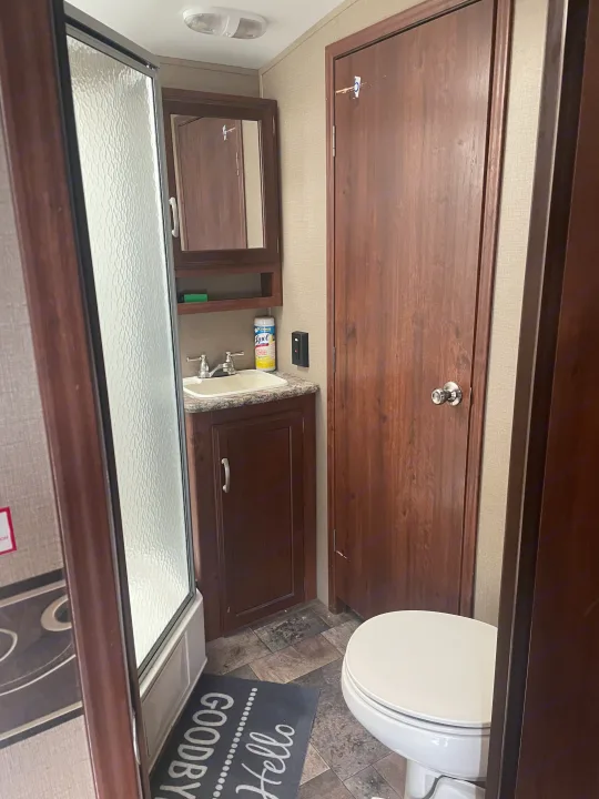 Inside a compact RV rental bathroom, featuring a textured glass shower, sink vanity, and toilet.. Keystone 316-UL 2014