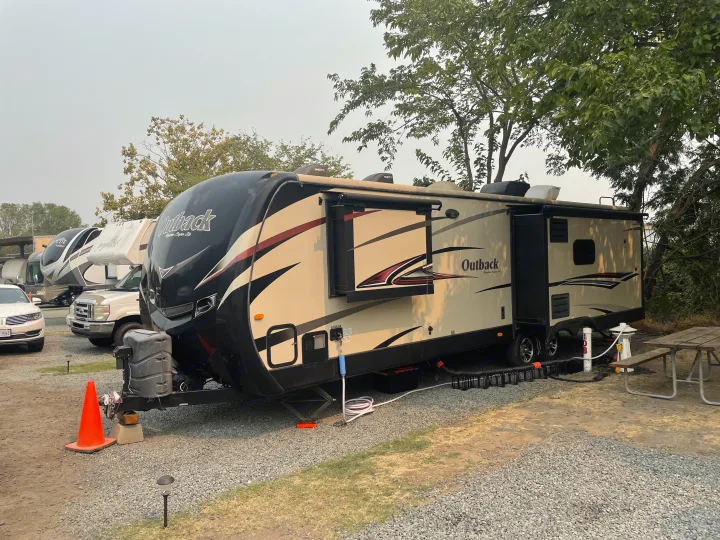 This Outback travel trailer RV rental is fully set up at a gravel campsite, with extended slide-outs & hookups.. Keystone 316-UL 2014