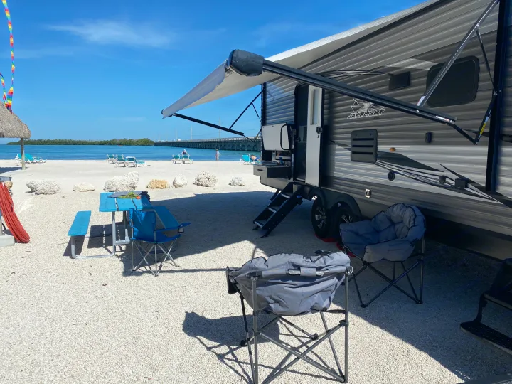 Perfect RV rental setup! Travel trailer with awning on a sunny, white gravel beach. Enjoying the blue water, chairs, & bridge view.. Jayco Jay Flight 2020