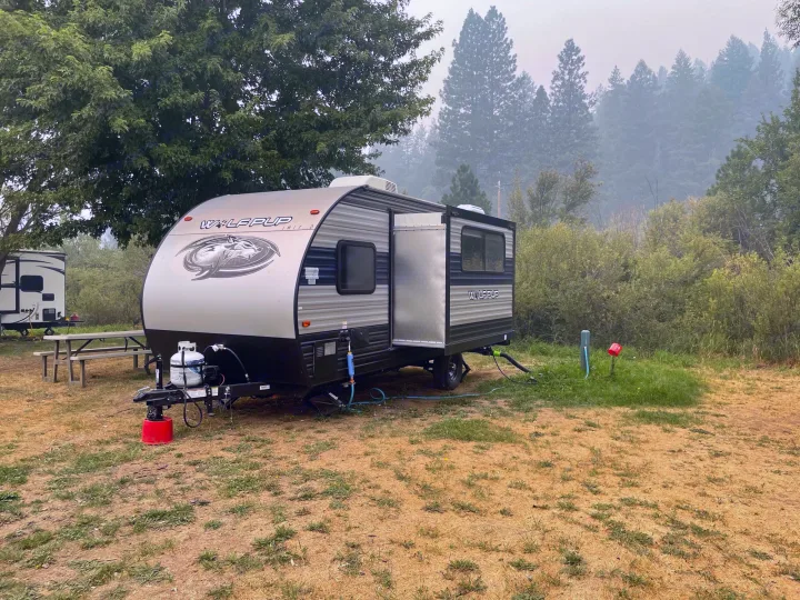 A Wolf Pup travel trailer, perfect as an RV rental, is set up at a dusty campsite with hazy forest views for outdoor camping.. Forest River Cherokee Wolf Pup 2020