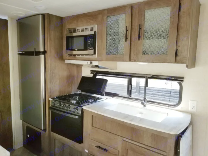 Inside an RV rental: compact kitchen with stainless fridge, microwave, stove, and sink.. Forest River Salem Cruise Lite 2021