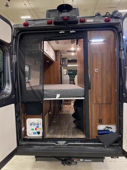 View inside a modern rv rental, highlighting smart storage, a bed, and water/electrical controls from the rear.. Winnebago Travato 2022