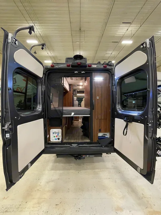 Open rear doors of a modern RV rental reveal a versatile interior, perfect for camping. See kitchen, bed, & storage.. Winnebago Travato 2022