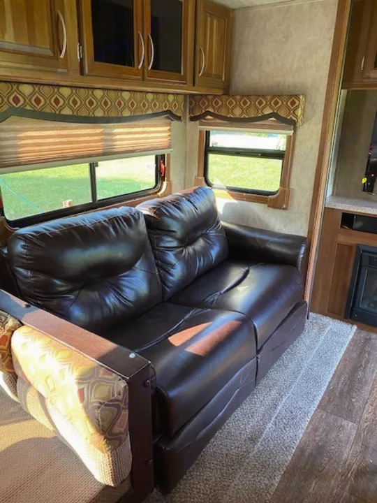 Spacious RV rental living area featuring a comfortable brown leather sofa, large windows, and ample wooden cabinets.. Forest River Crusader BH 2015