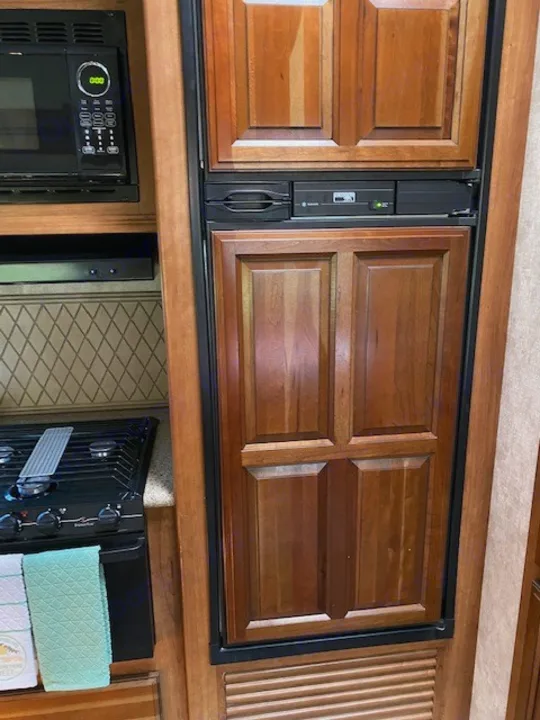 Inside an RV rental: Compact kitchen featuring a microwave, two-burner gas stove, and a wood-paneled refrigerator/freezer.. Forest River Crusader BH 2015