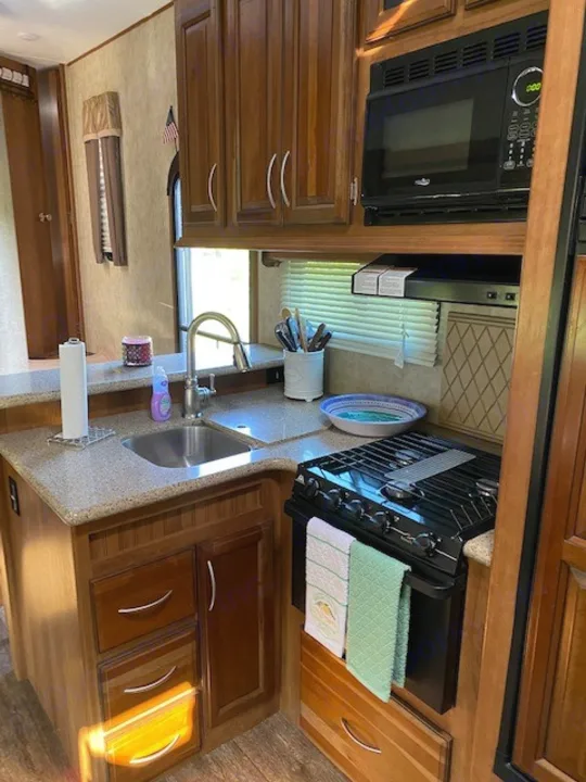 RV rental kitchen: Wood cabinets frame a compact space with sink, microwave, and stovetop.. Forest River Crusader BH 2015