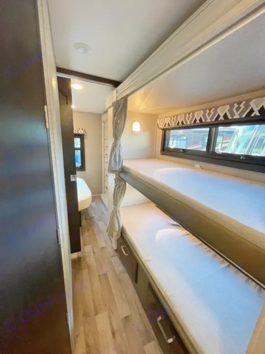 Inside an RV rental, showing a multi-level bunk bed sleeping area with storage and windows for travel.. Jayco Redhawk 2022