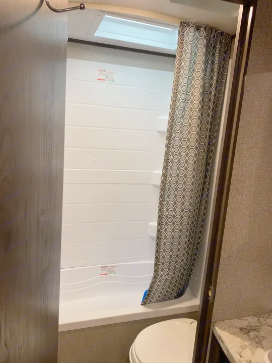 This RV rental bathroom features a clean white shower with a geometric curtain, skylight, and toilet.. Jayco Flight 2021