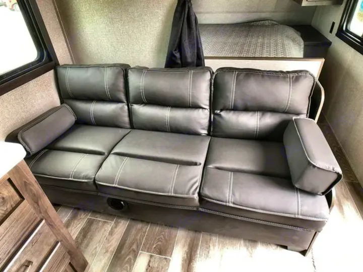 Inside an RV rental: a gray, three-seat sofa with white stitching, perfect for relaxing after a day's travel.. Jayco Flight 2021
