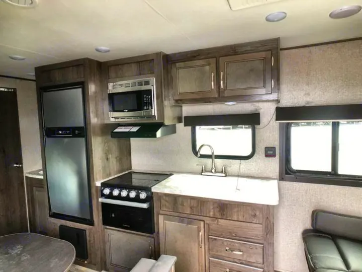 Inside a modern RV rental, featuring a full kitchen with fridge, stove, microwave, and sink amidst wood-tone cabinets.. Jayco Flight 2021