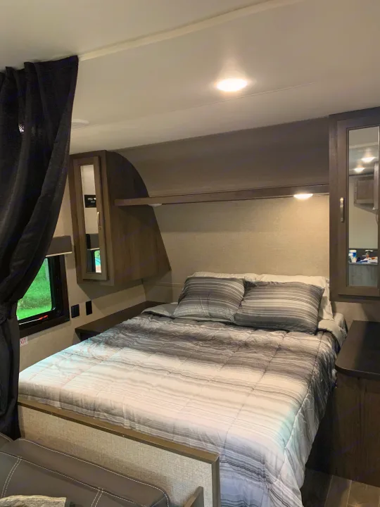 Cozy RV rental bedroom showcasing a striped bed, built-in storage, and window, designed for comfortable travel.. Jayco Flight 2021