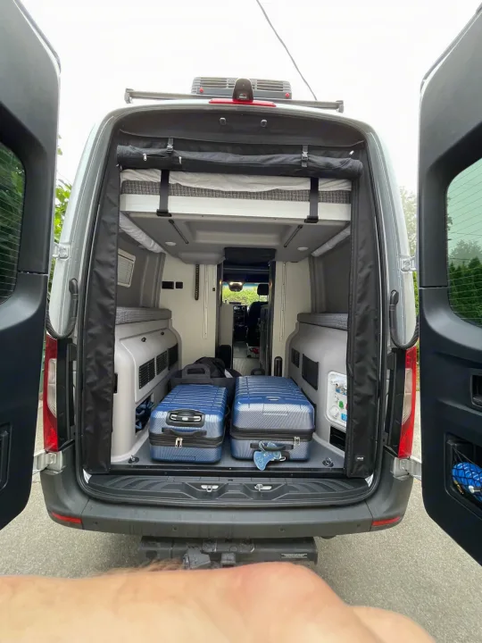 RV rental interior: ready for travel with luggage, a compact bed, and van amenities visible from the open back.. Winnebago Revel 2021