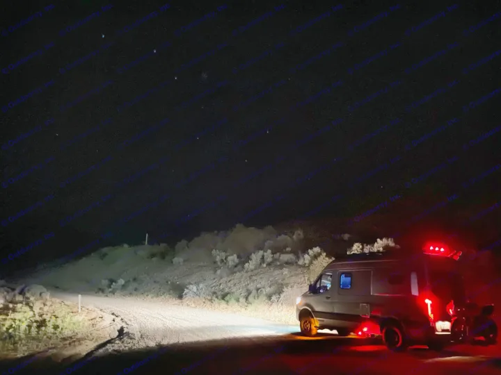 A an RV rental van with glowing red lights on a desert dirt road under faint stars at night. Perfect for dark sky camping.. Winnebago Revel 2021