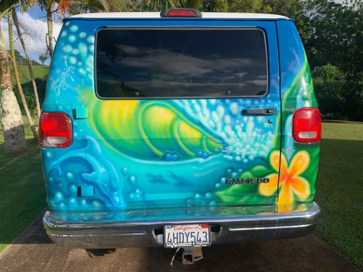 Eye-catching RV rental: a custom-painted blue Ram 1500 van featuring a vibrant surf and wave mural on its rear.. Dodge Ram 1500 1999