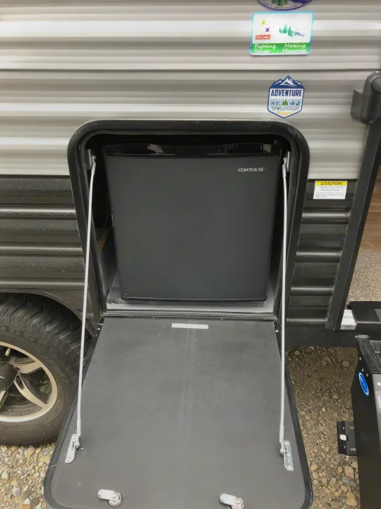 Open exterior compartment of an RV rental revealing a Contoure mini-refrigerator, useful for camping.. Forest River Wolf Pup 2021