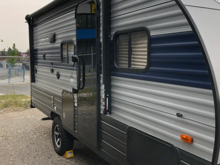 A grey and blue Wolf Pup travel trailer, featuring a 12V power awning, parked on gravel. Ideal for rv rental.. Forest River Wolf Pup 2021
