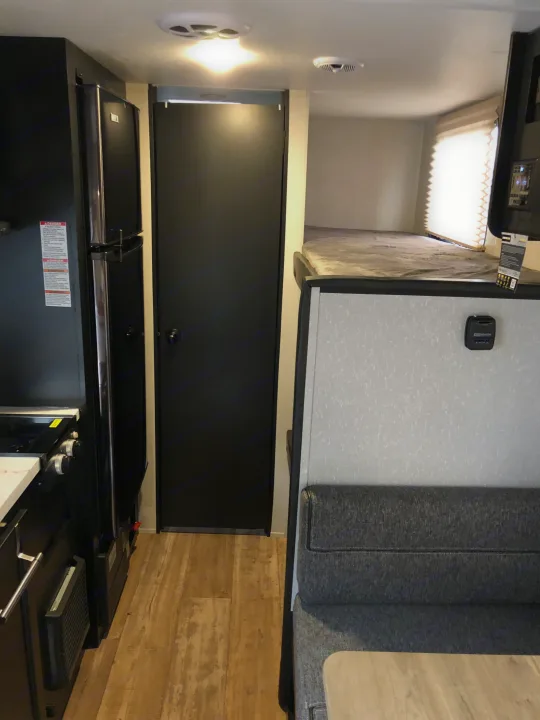 Inside an RV rental, this view shows the kitchen with a black refrigerator, a dark door, and bunk beds above a dinette.. Forest River Wolf Pup 2021