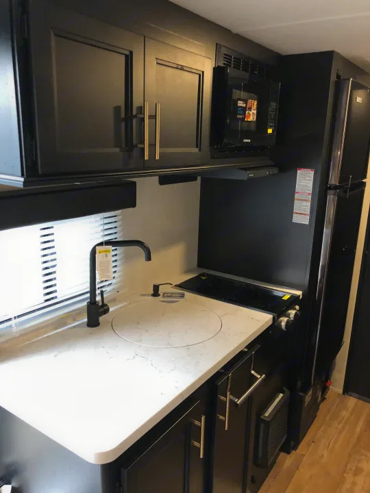 Explore this compact RV rental kitchen featuring a modern sink, stovetop, microwave, and refrigerator in sleek black and white.. Forest River Wolf Pup 2021