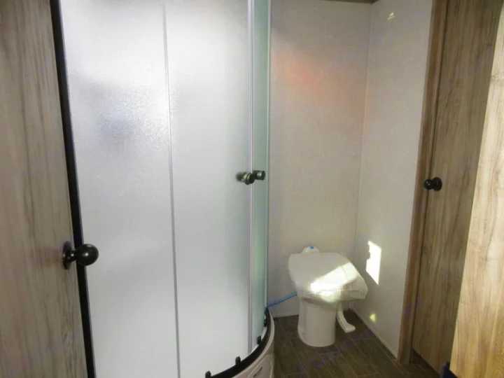 Compact RV rental bathroom features a frosted glass shower, covered toilet, and wood-look flooring.. Forest River 30DBH-L 2021