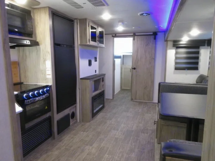 Explore this modern RV rental interior: kitchen with microwave, oven, fridge, dining booth, and a barn door hallway.. Forest River 30DBH-L 2021