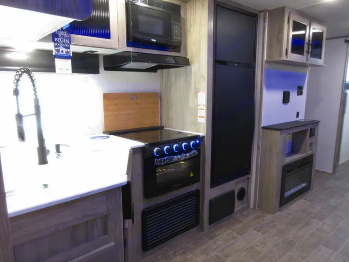 Modern RV rental interior with a bright kitchen, featuring a sink, microwave, oven, refrigerator, and an electric fireplace.. Forest River 30DBH-L 2021