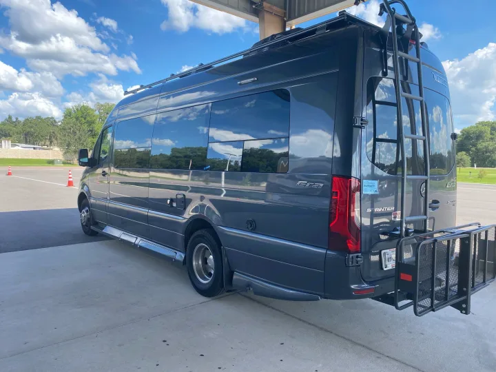 Dark gray Mercedes-Benz Sprinter Era RV rental features a roof rack, ladder, and rear cargo carrier, parked outdoors.. Winnebago Era 2021