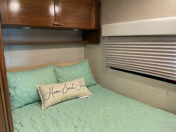 Cozy RV rental bedroom featuring mint green seashell bedding, "Home Sweet Home" pillow, and wooden cabinets above the bed.. Winnebago Outlook 2020
