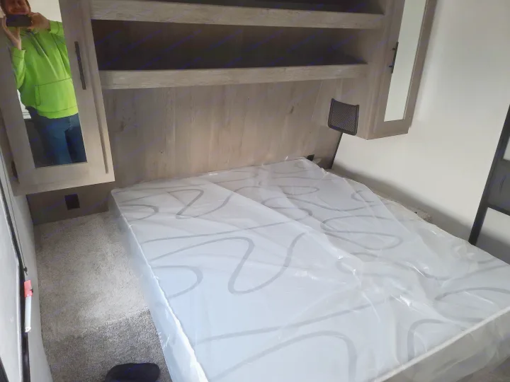 Experience comfort in this RV rental bedroom. It features a new, plastic-covered mattress, built-in shelving, and carpeted floors.. Keystone Springdale 2021