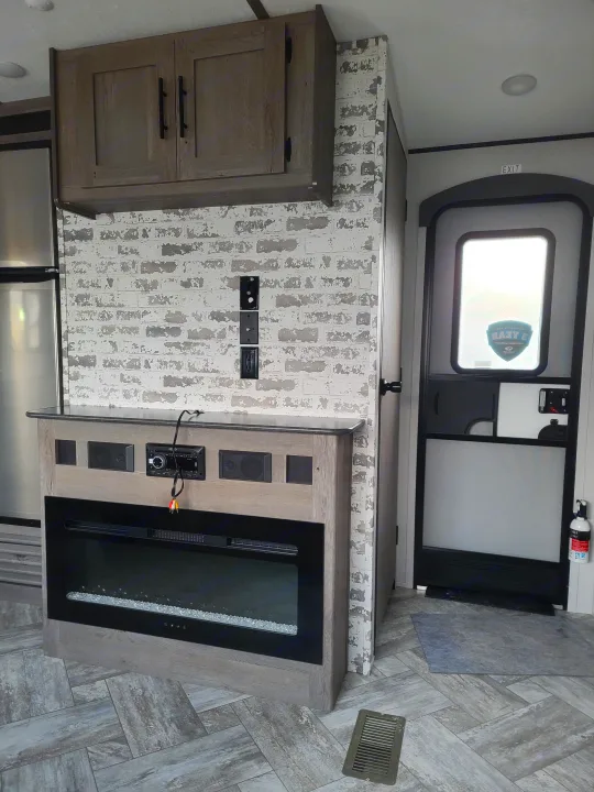 RV rental interior: Modern living space featuring an electric fireplace, entertainment center, cabinets, and entrance door.. Keystone Springdale 2021