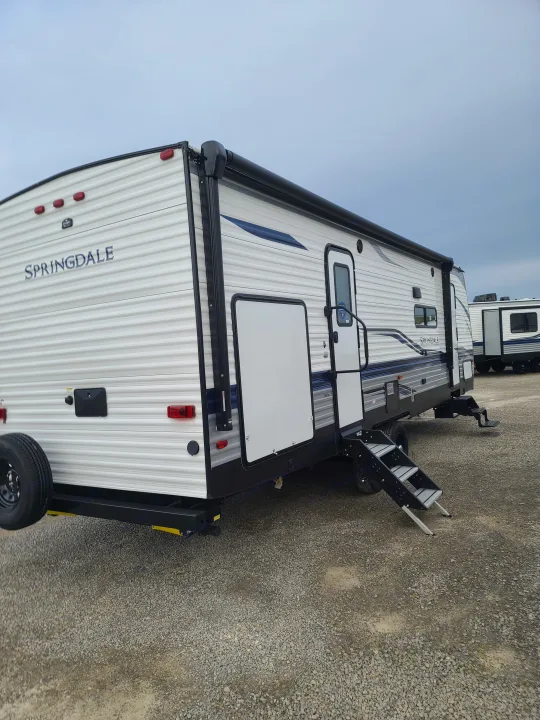 This RV rental is a white and blue Springdale travel trailer with an awning and steps, parked on gravel. Ideal for adventures!. Keystone Springdale 2021