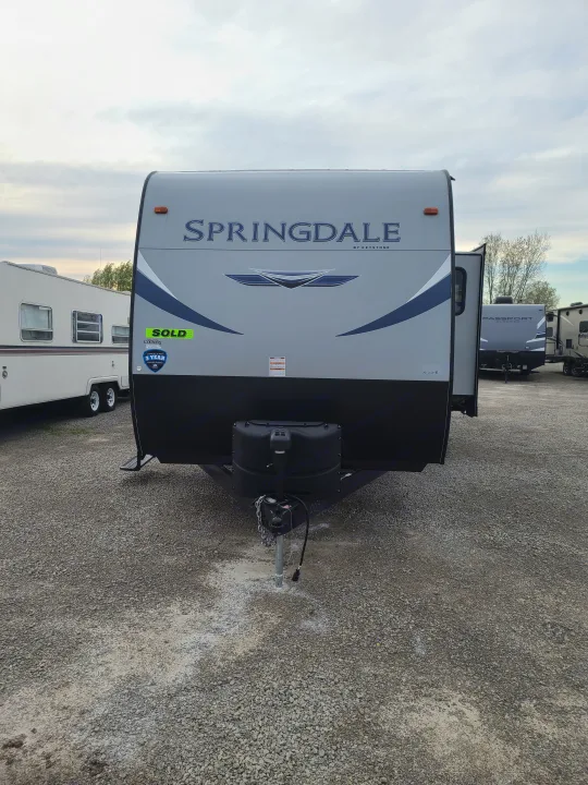 A gray Springdale travel trailer, marked SOLD, is on a gravel lot at an RV dealership. Perfect for RV rental inspiration.. Keystone Springdale 2021