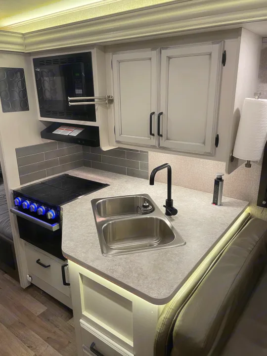 Bright, modern RV rental kitchen features microwave, stove, sink, ample cabinets, and task lighting for your journeys.. Jayco Redhawk 2021