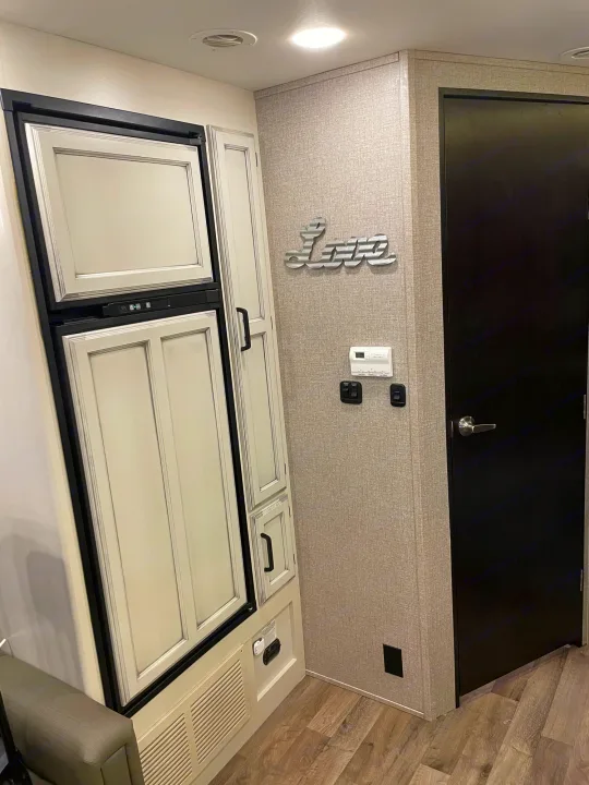 RV rental interior: Light-paneled fridge, storage, wall controls, "Love" decor, and door on wood-look floor.. Jayco Redhawk 2021