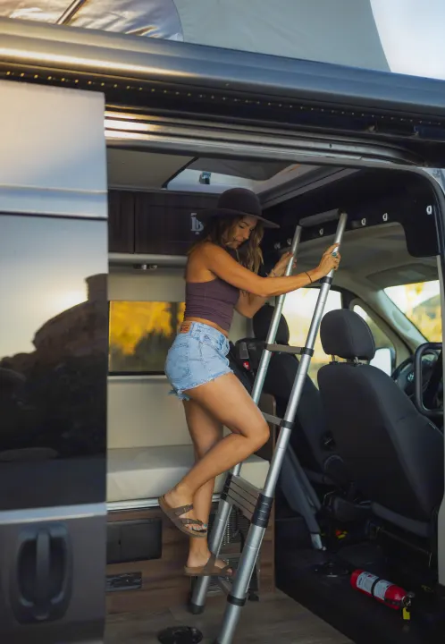 Woman climbing ladder in RV rental to reach the pop-top bed of this modern camper van.. Hymer Axion Other 2019