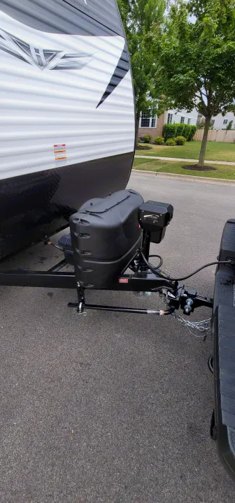 Hitch area of an RV rental: travel trailer connected for towing, showing propane tanks, electric jack, and weight distribution system.. Keystone Hideout 2021