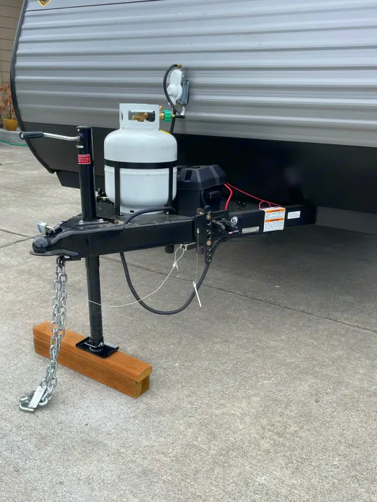 RV rental's front assembly featuring the hitch, leveling jack on wood, dual propane tanks, and battery box on concrete.. Other Other 2021