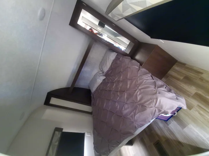 Explore this RV rental's bedroom: cozy bed, wood flooring, storage, and a mirror showing a person. Great mobile accommodation.. Forest River Salem 2019