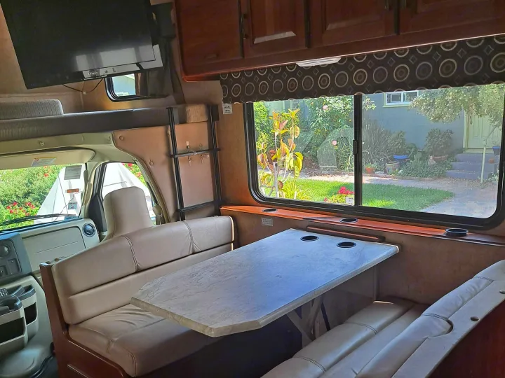 Spacious RV rental interior with dinette, bunk, and large windows, offering comfortable living space for your road trip.. Forest River Sunseeker 2018